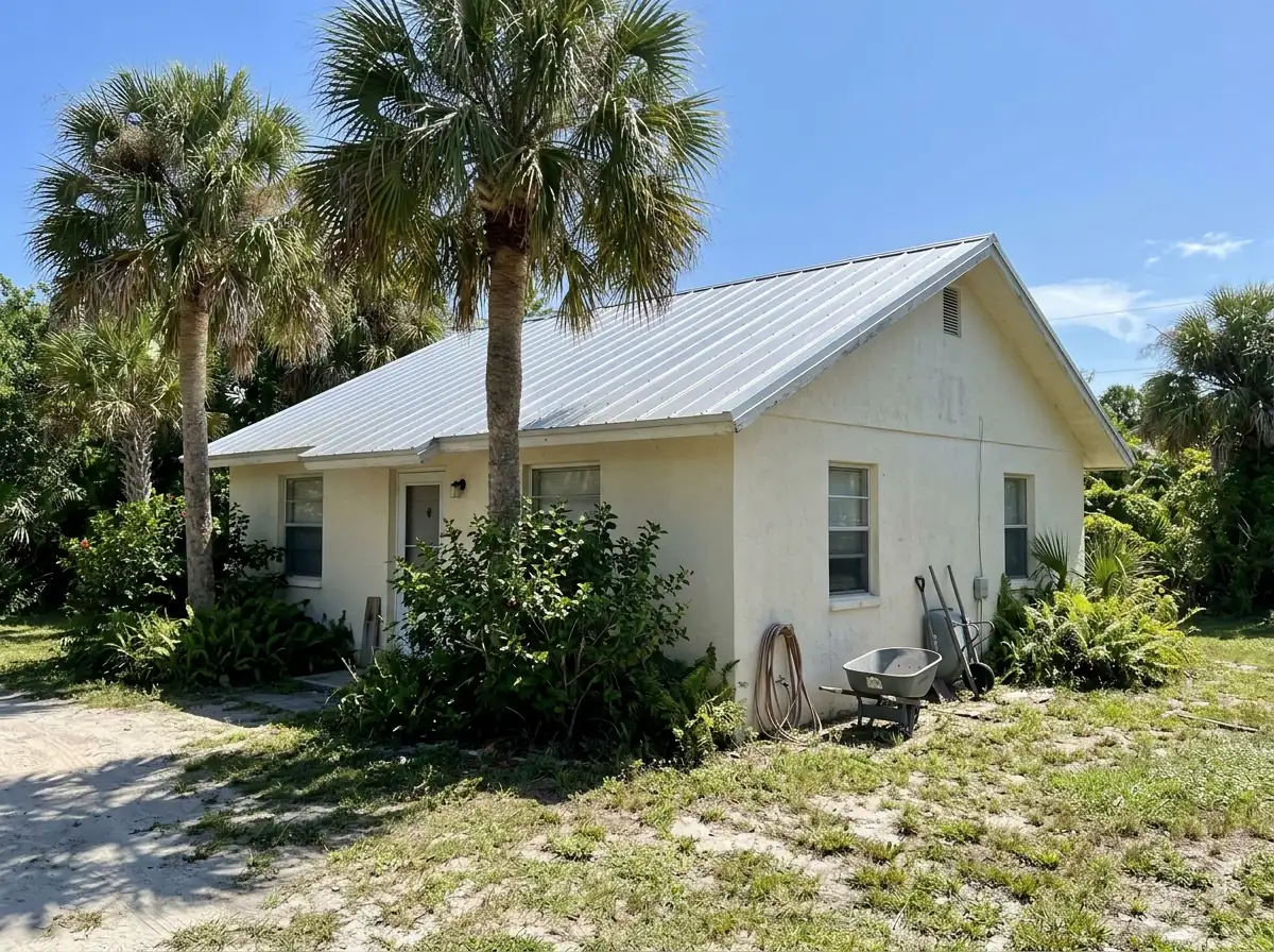 Silver unpainted 5V crimp metal roof on a small stucco cottage with palm trees