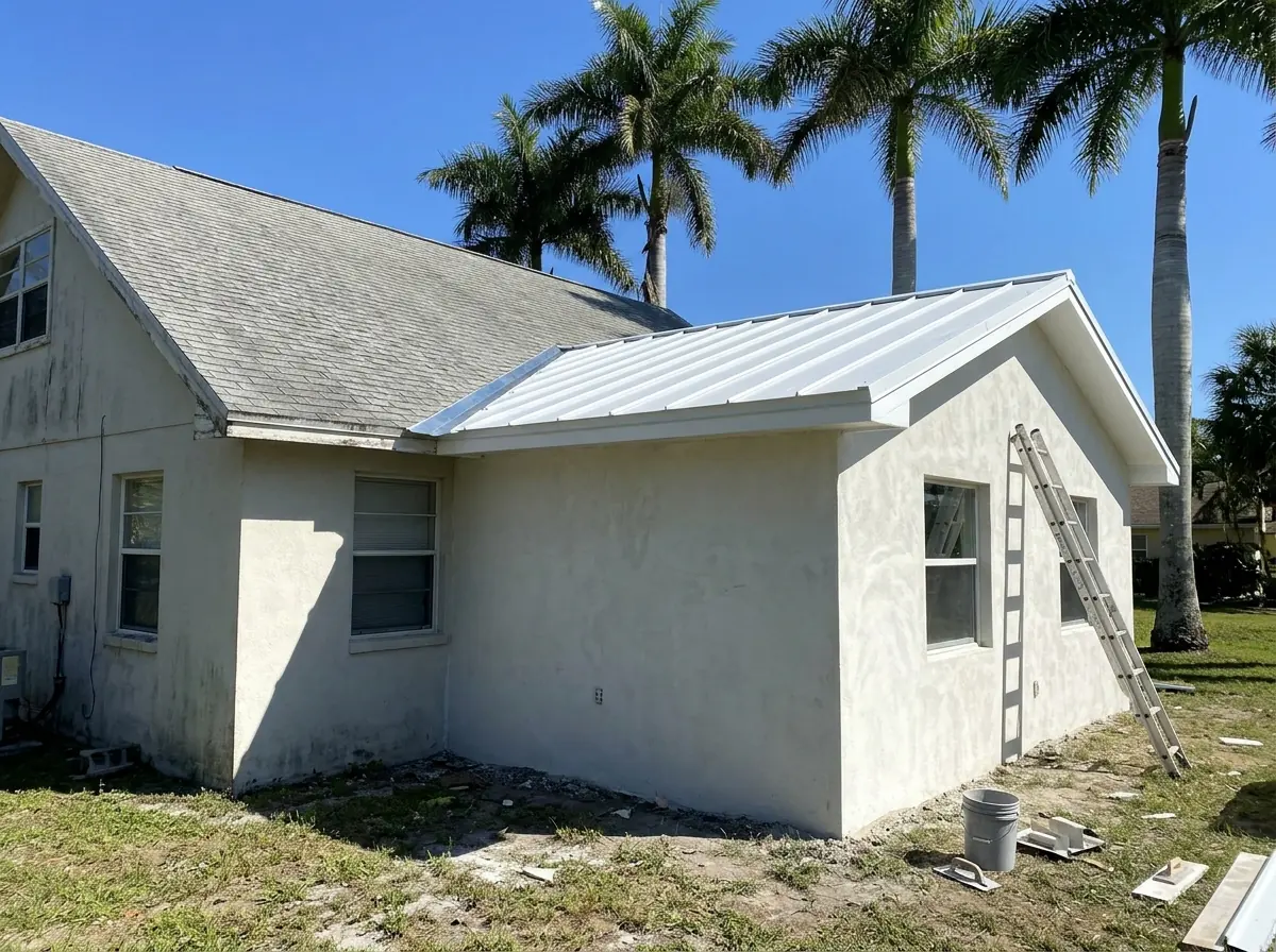 New metal roof on a single-story room addition meeting the edge of an older roof, with fresh metal flashing at the joint