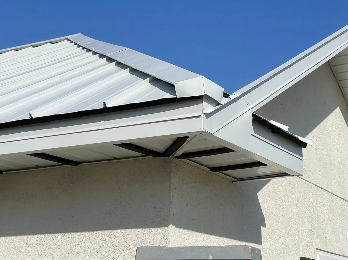 Close view of a white metal drip edge and rake trim along a roof edge, with foam closures filling the panel ribs at the eave