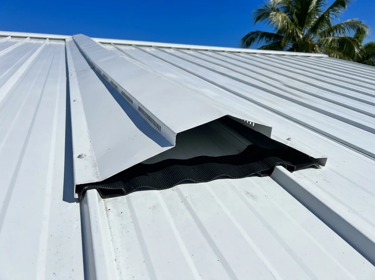 Vented ridge cap along the peak of a white standing seam metal roof with a profiled closure strip visible at the open end
